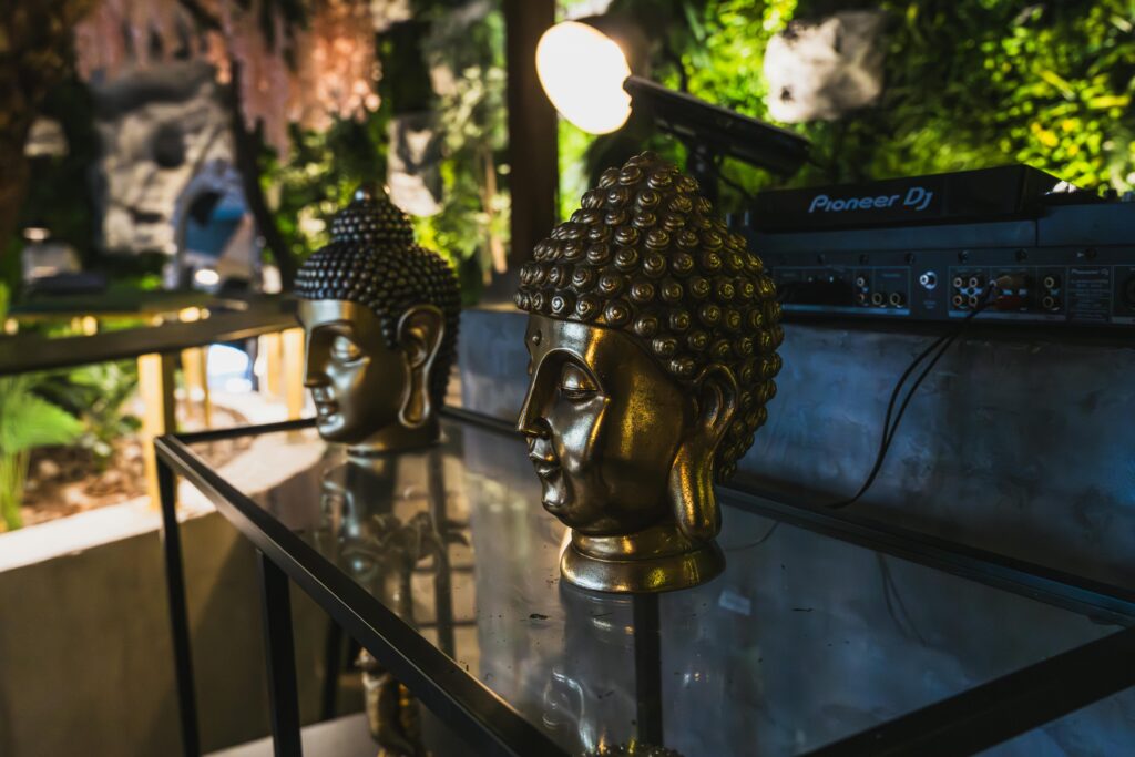 Illuminated golden Buddha heads on tables next to DJ setup in ambient indoor settings.