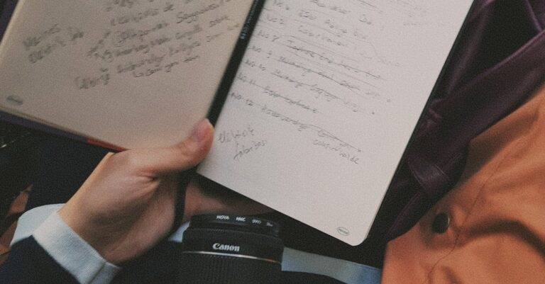A person holding a notebook with handwritten notes and a camera in view, symbolizing creativity and travel.