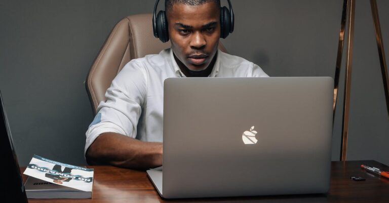 Professional man wearing headphones, working intently on a laptop in a modern office setting.