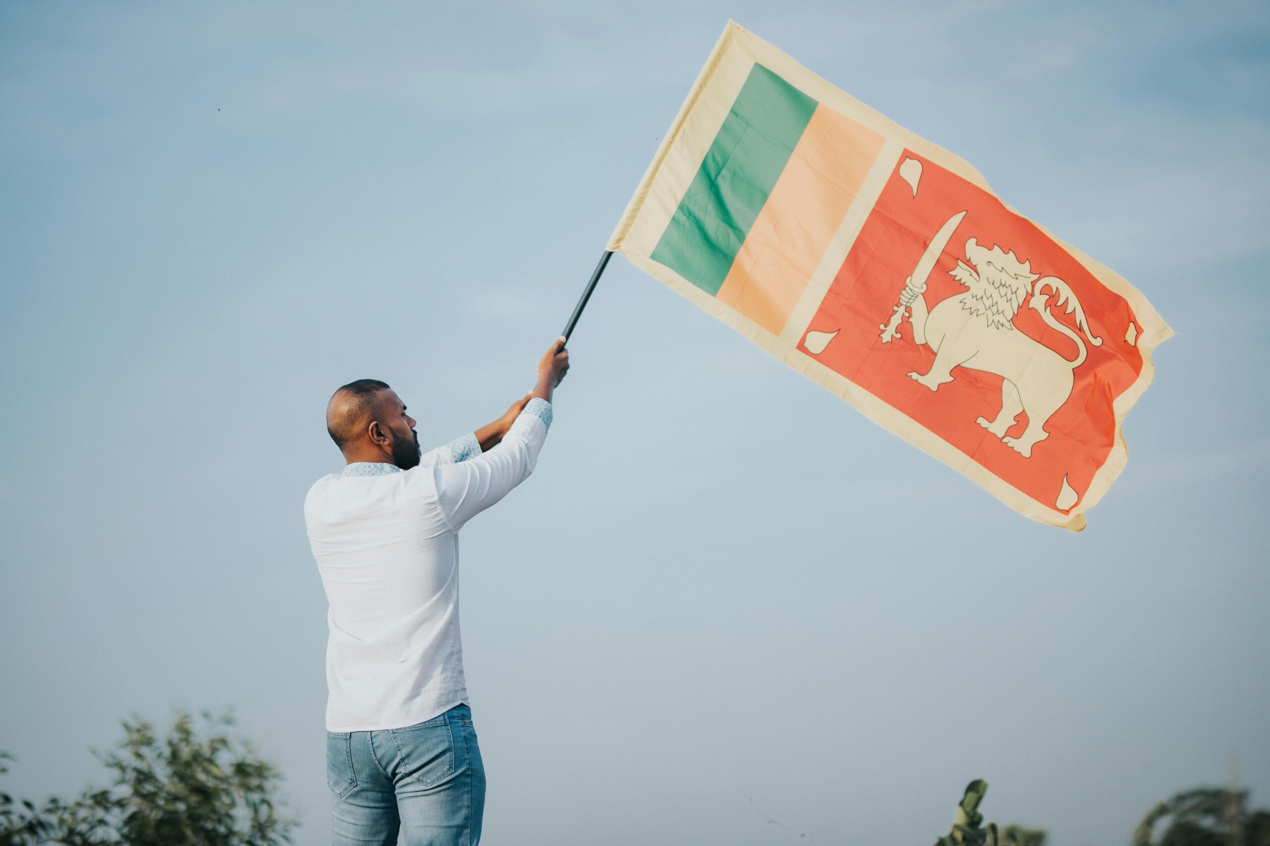 A man proudly waves the Sri Lankan flag outdoors under a clear blue sky, symbolizing national pride.
