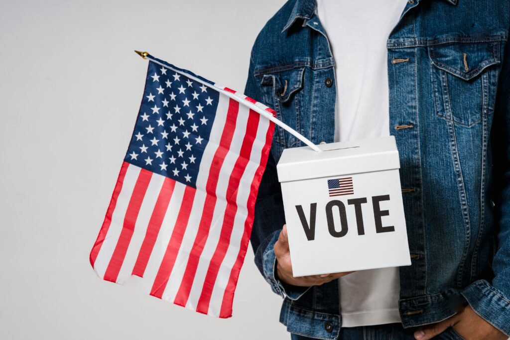 Man holding an American flag and a vote box symbolizing democratic participation.