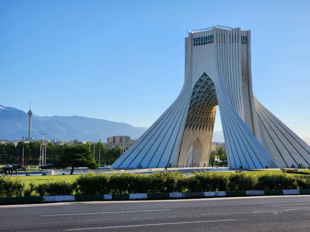 Capture of the iconic Azadi Tower in Tehran with a mountainous backdrop and clear sky.