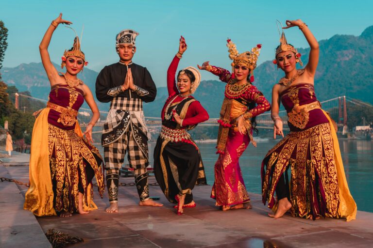 Traditional dancers in vibrant costumes perform by a river in Rishikesh, India, showcasing cultural heritage.