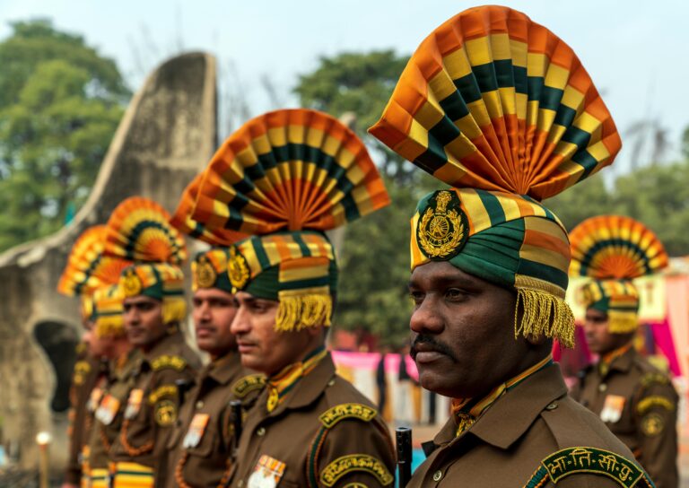Indian soldiers in ceremonial uniforms with ornate headdresses standing outdoors.