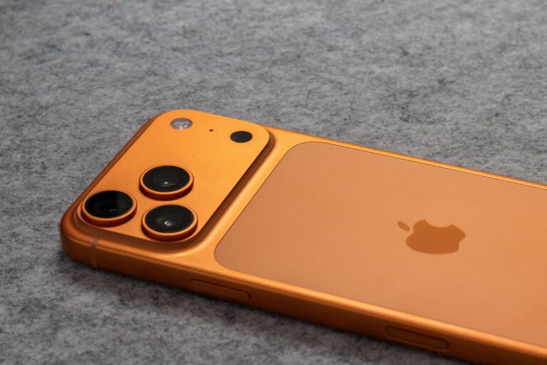 Orange smartphone with dual cameras placed on a soft gray fabric surface.