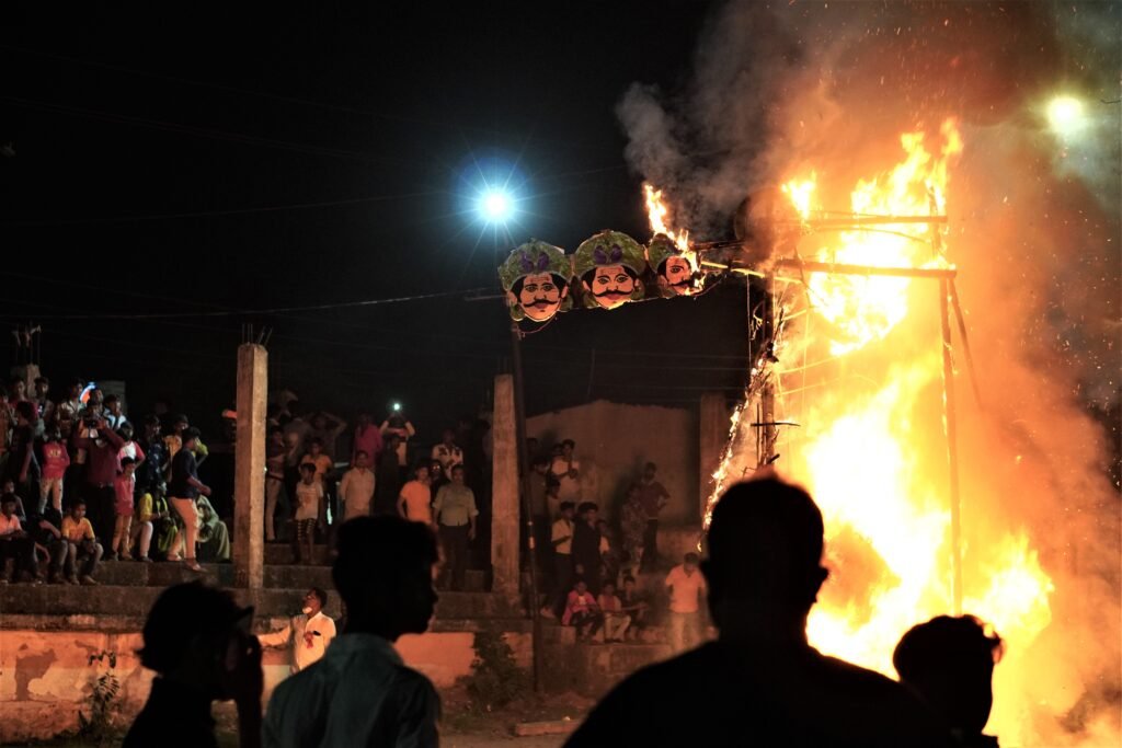Crowd gathers at night for a festival celebration with a massive effigy burning in a vibrant display.